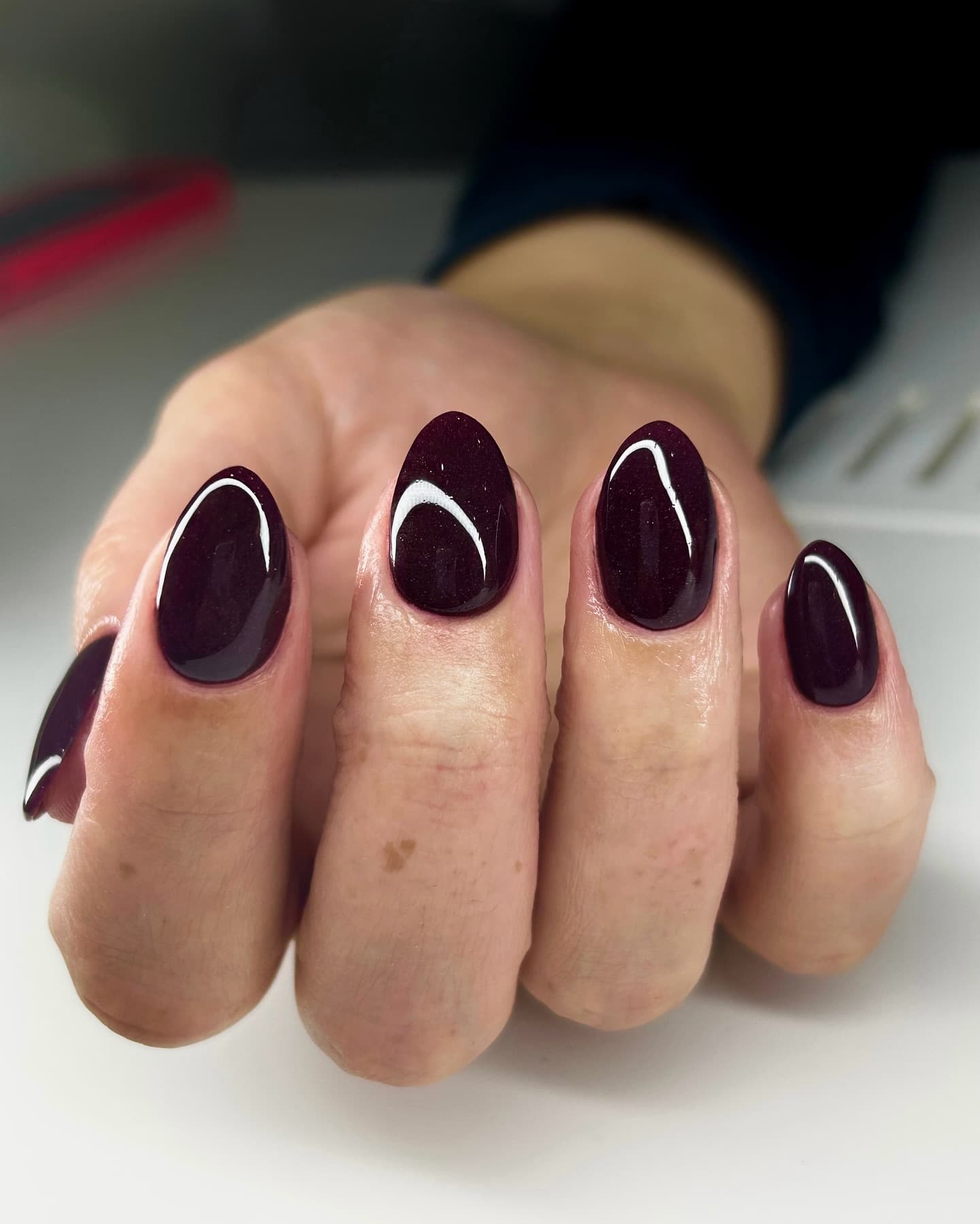 Deep burgundy almond gel nails with a white swirl accent