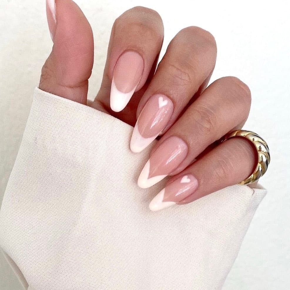 Nude French tips with a hand-painted white heart accent on almond-shaped nails