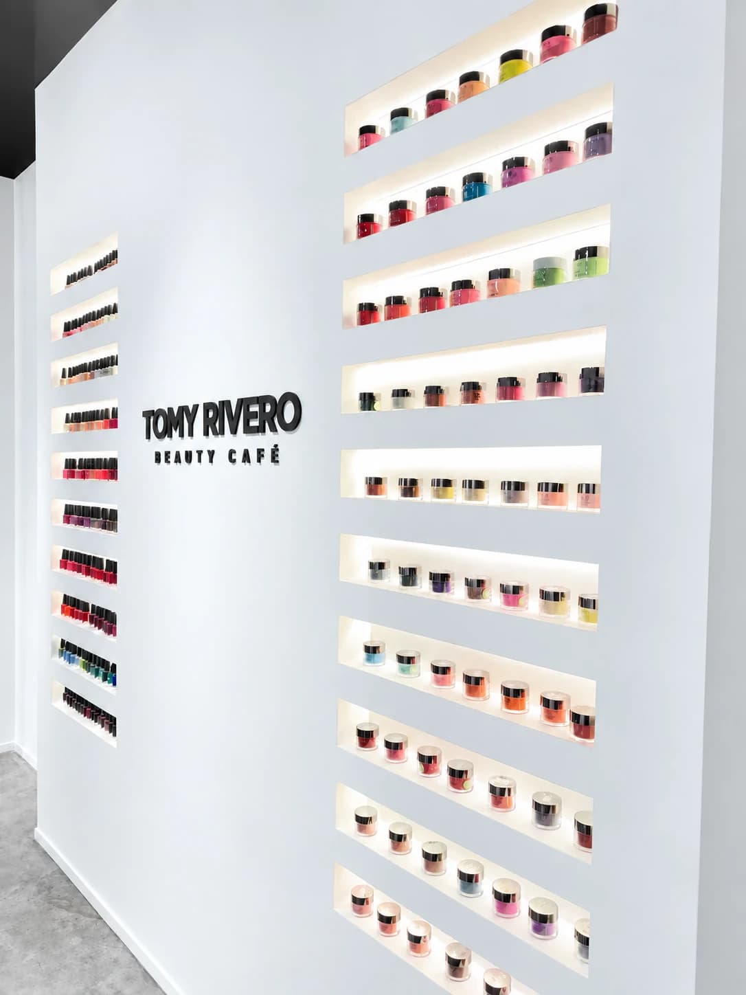 Tomy Rivero Beauty Cafe wordmark mounted between the illuminated nail polish shelves
